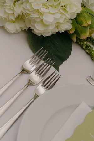 Close-up of white hydrangeas and place settings with silver cutlery on a pristine tablecloth.