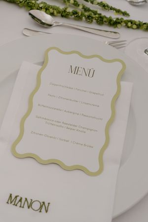 Wedding menu card with gold trim and elegant typography displayed on a white table setting.