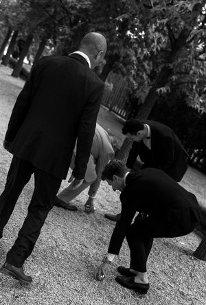 Black and white photo of wedding guests' feet and legs on gravel path during reception.