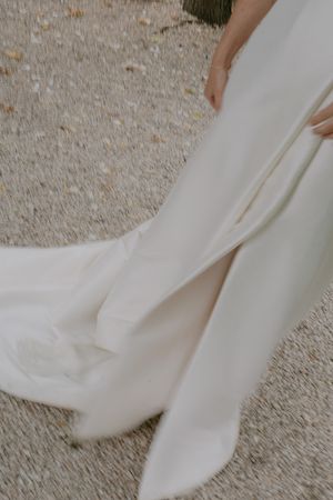 Close-up detail shot of flowing white wedding dress fabric against gravel ground.