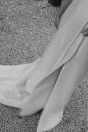 Black and white detail shot of wedding dress hem trailing on gravel pathway.