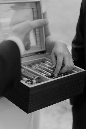 Black and white close-up of hands opening decorative wooden box at wedding event.