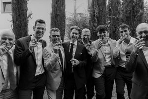 A group of groomsmen in formal attire share laughs at an outdoor gathering.