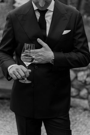 A close-up of a suited guest holding a wine glass at an outdoor event.
