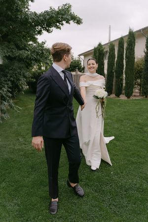 Candid wedding photo of couple walking and laughing on lawn with cypress trees in background.