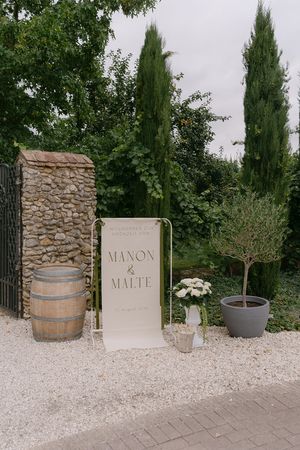 Rustic wedding decor featuring stone walls, wooden barrels, and signage on white gravel path.