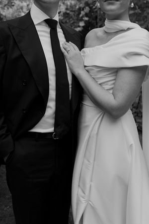 Close-up detail shot of bride in off-shoulder dress and groom in classic black suit.