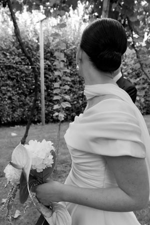 Back view of bride wearing elegant white dress with off-shoulder detail and holding bouquet.