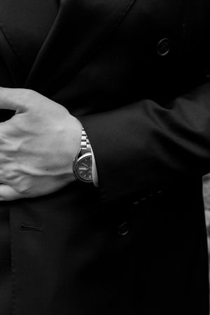 Detail shot of metal watch on wrist against dark suit fabric.