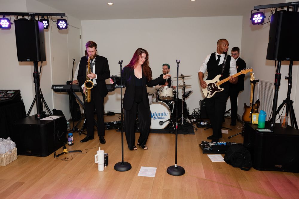 Musicians performing on stage with instruments while people dance in a spacious ballroom.