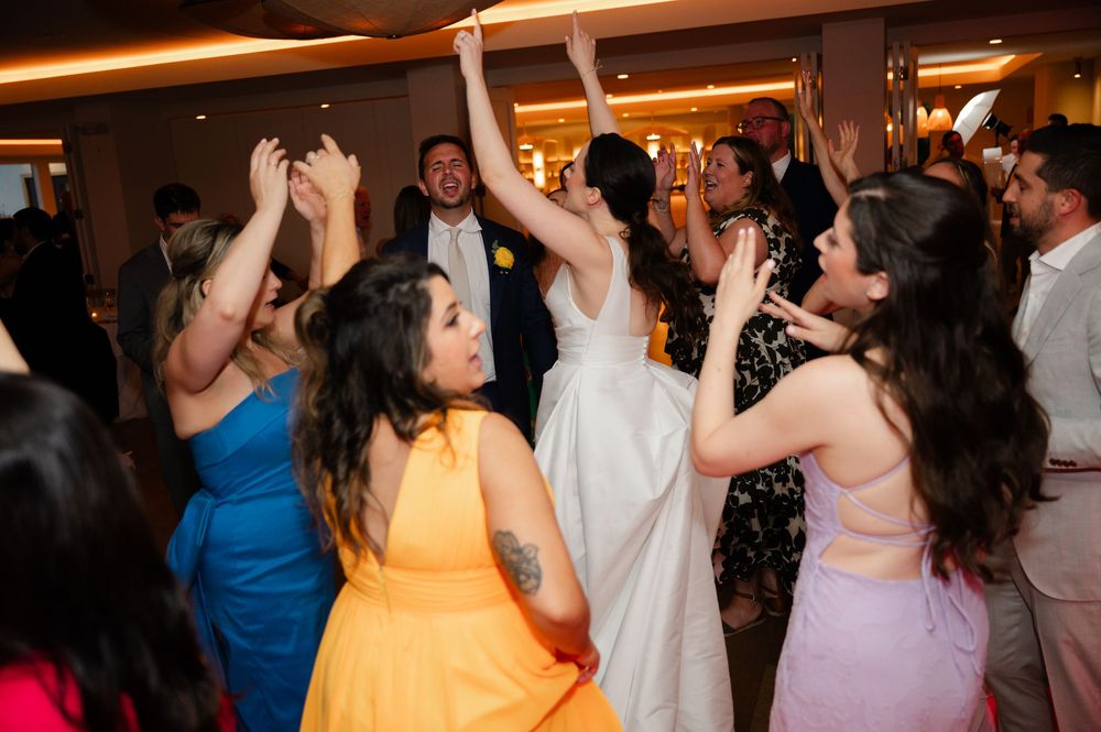 Dancing and celebrating crowd on a dance floor at a lively indoor party event under warm lighting.