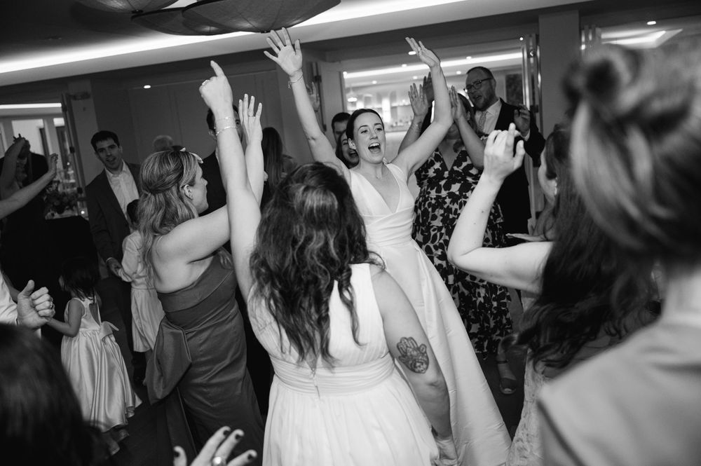 Wedding party guests dancing and celebrating with raised hands on a dimly lit dance floor at a reception party.