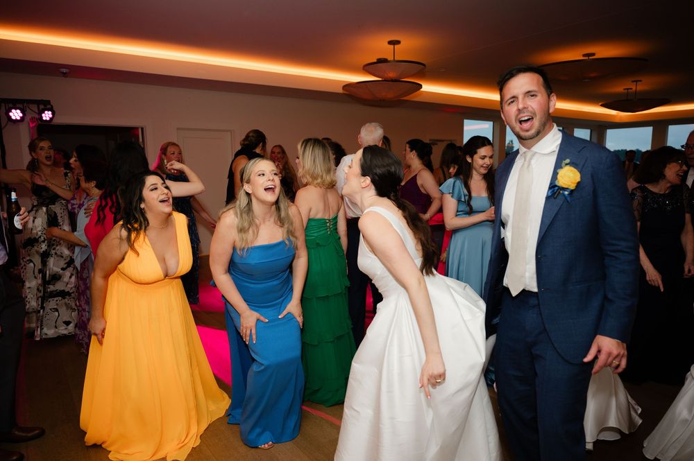 Wedding guests dancing and celebrating on a lively dance floor with colorful lighting effects.