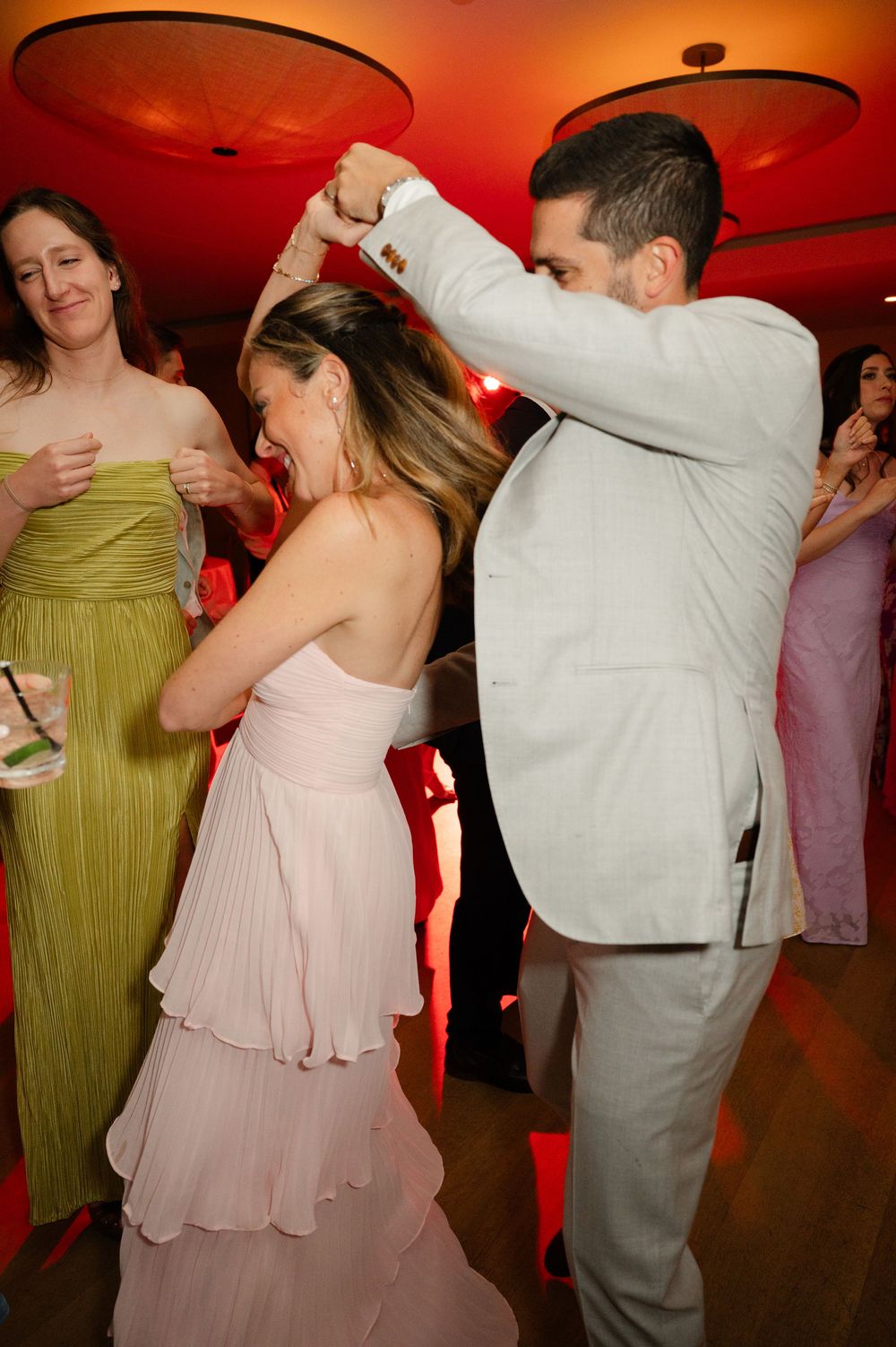 Couples dance together at a wedding reception under red ambient lighting while wearing formal attire.