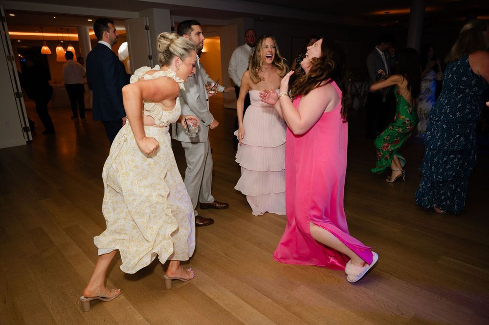 Wedding guests dance and celebrate together during an energetic reception party on a wooden dance floor.