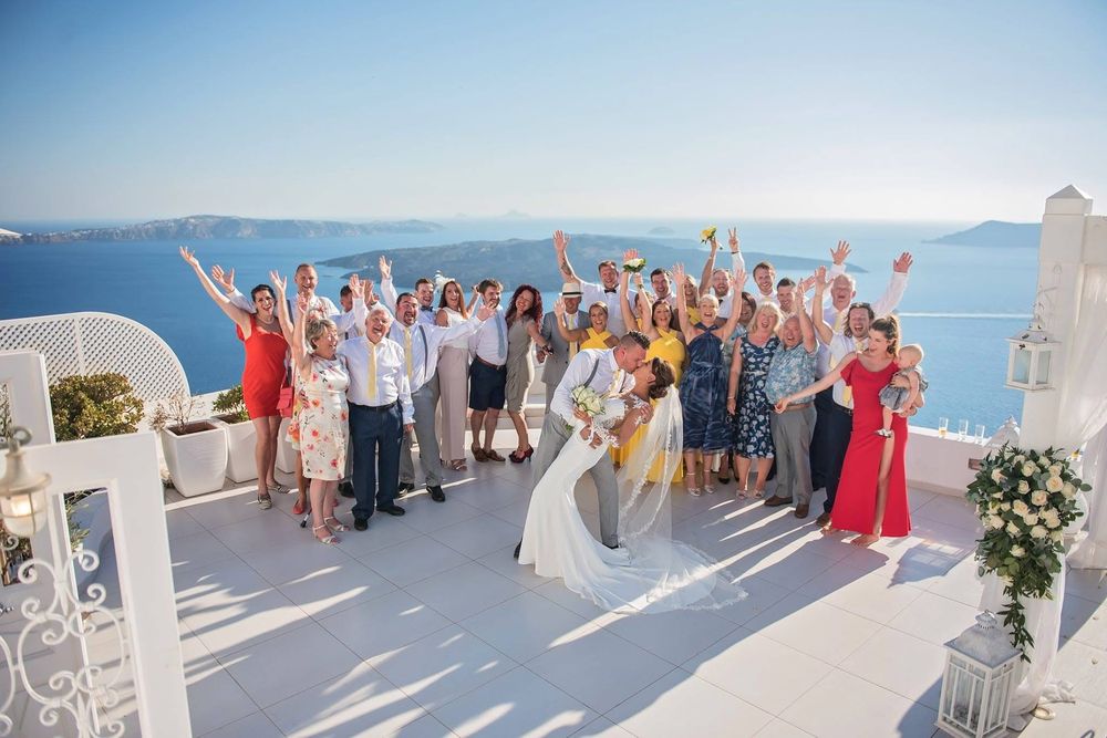 A series of wedding guests posing on a beautiful white terrace overlooking the blue ocean on a sunny day.