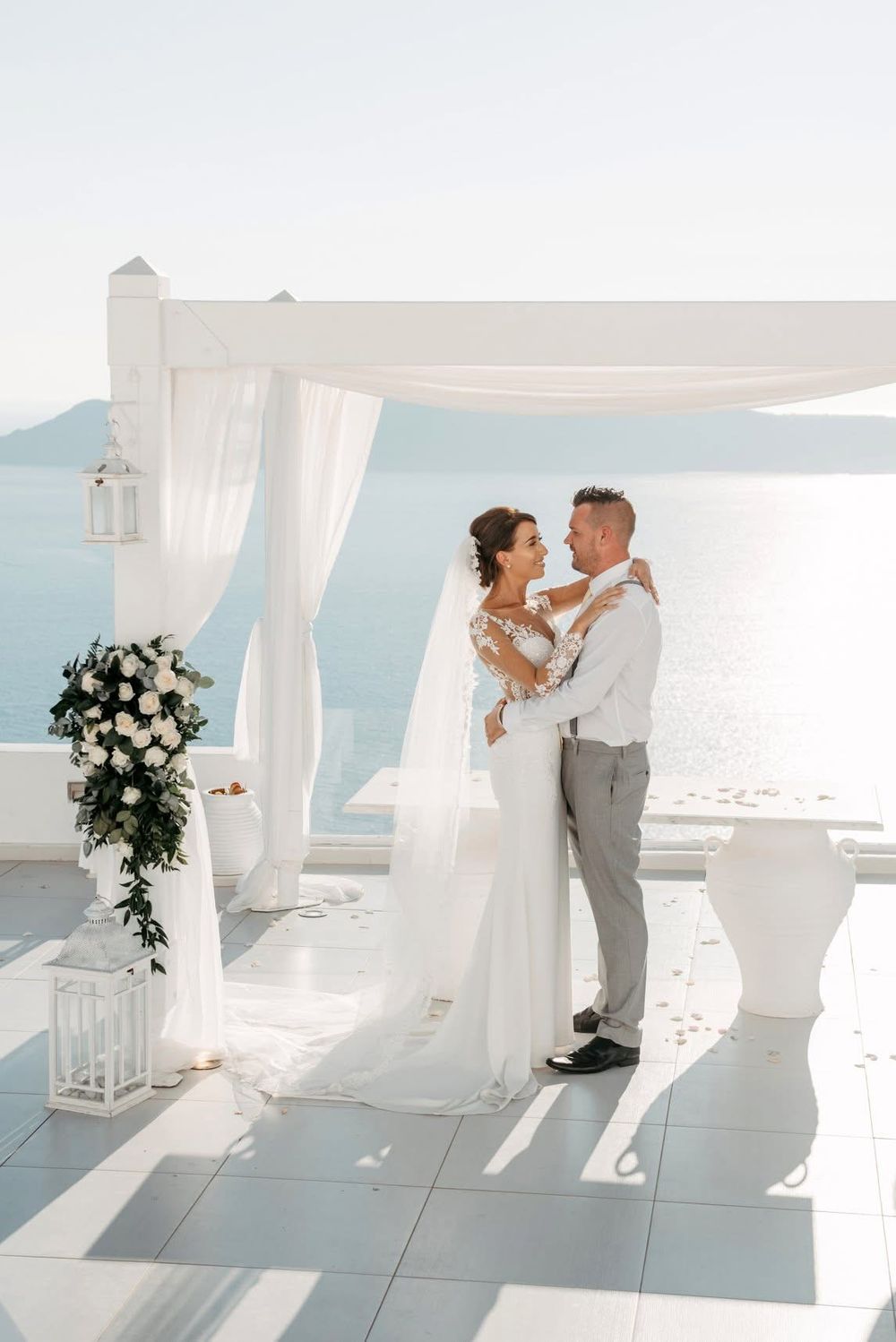 Couple embraces during their romantic oceanside wedding ceremony under a white canopy in Santorini.