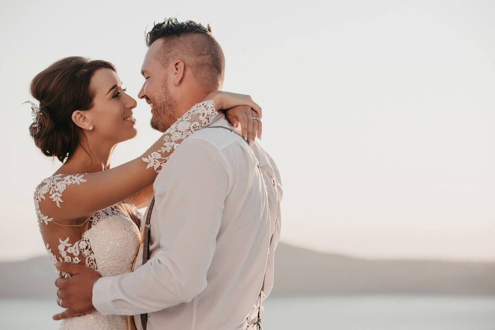 A romantic bridal couple embraces during sunset at a beach wedding ceremony.
