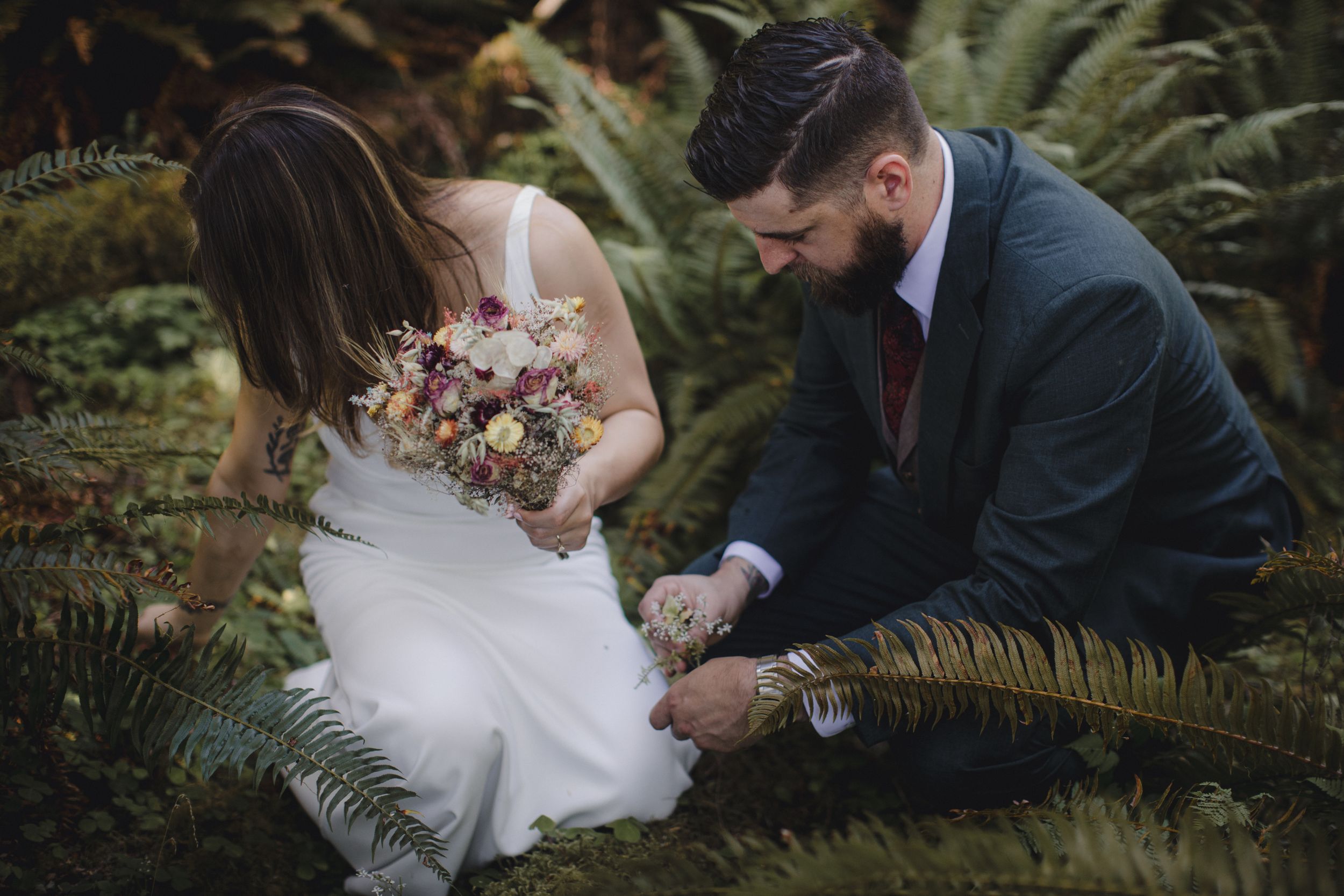 A couple sits together in a lush garden setting surrounded by ferns and greenery.