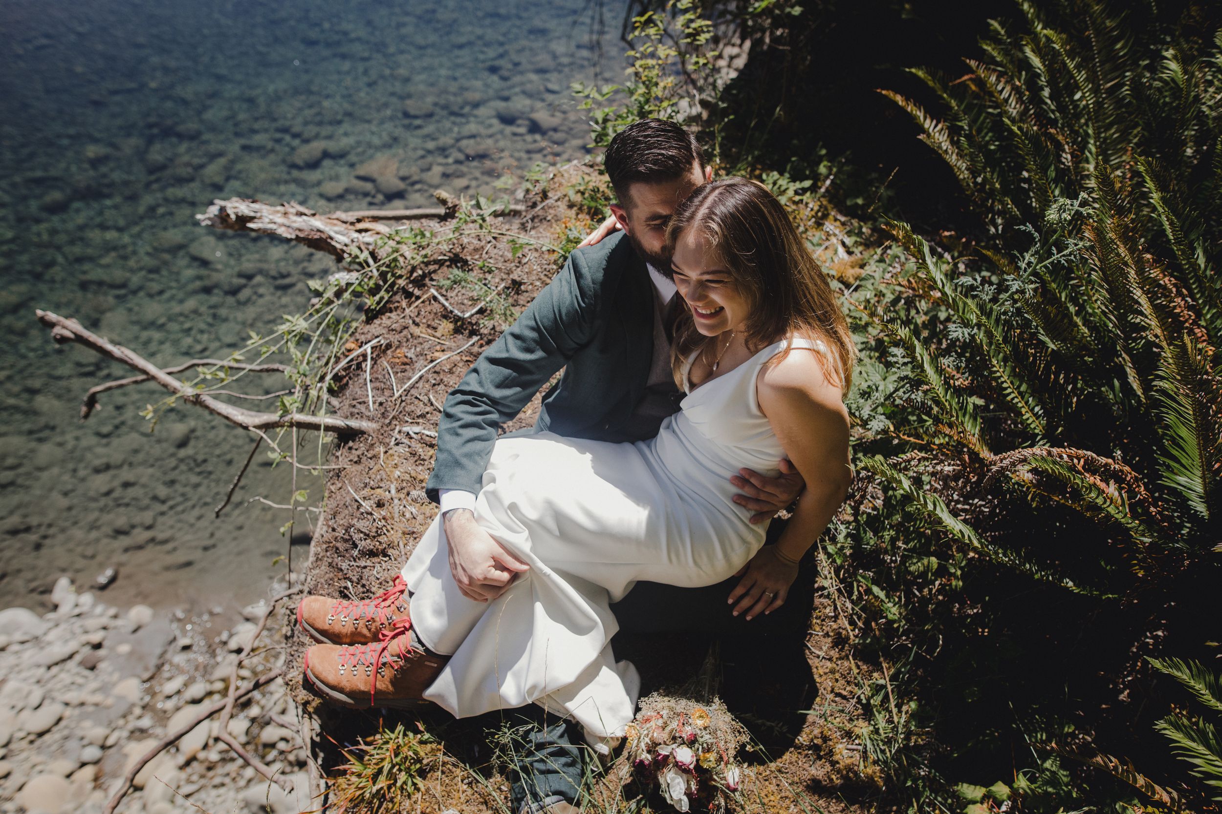Two people relax together on a rocky coastal overlook with bright blue ocean waters visible below.