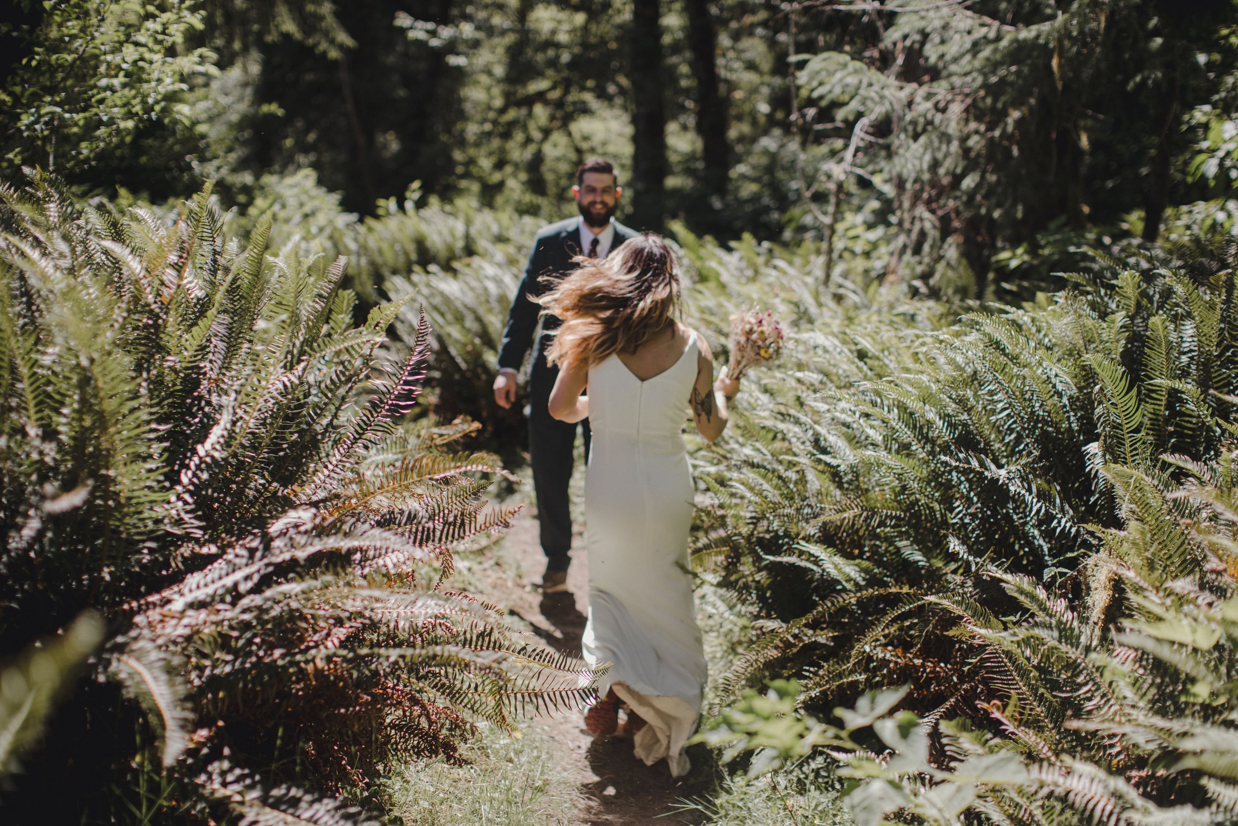 Person joyfully walking through a lush forest path with sunlight streaming through trees.