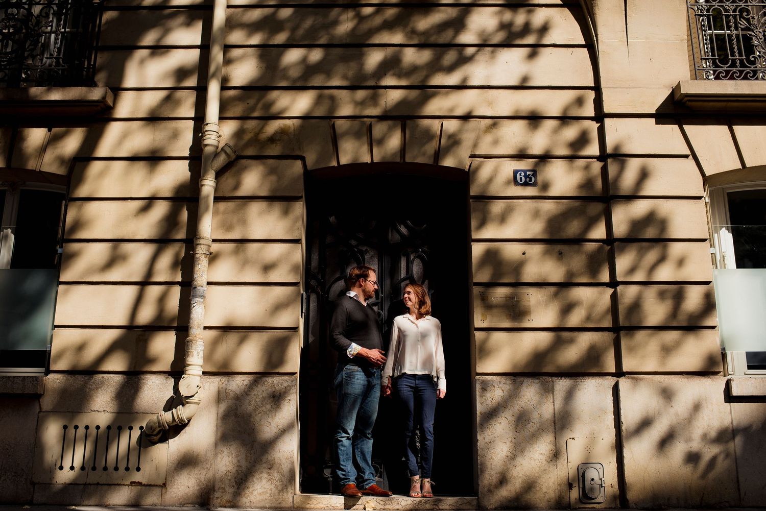Sunlight casts dramatic shadows on a building facade as a couple stands in a doorway.
