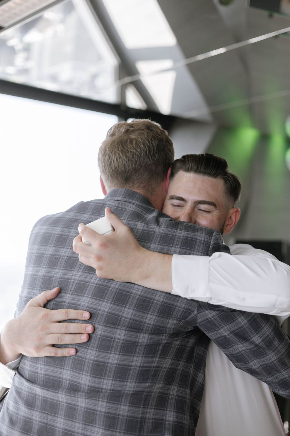 Two people in plaid and white shirts embracing in an emotional moment.