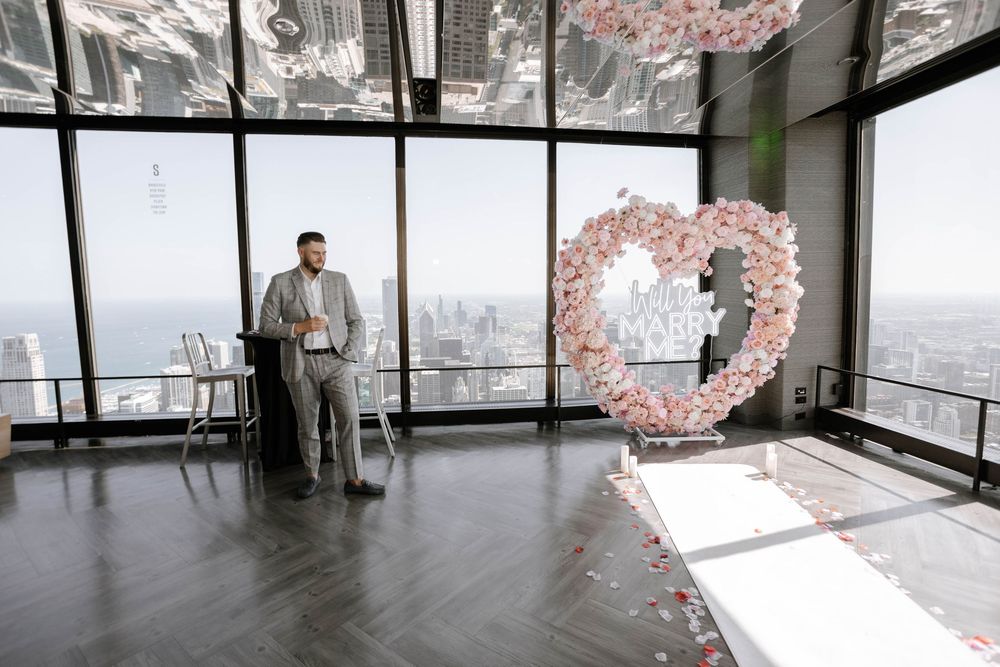 A panoramic view of a modern event space with floor-to-ceiling windows and delicate pink floral arrangements.