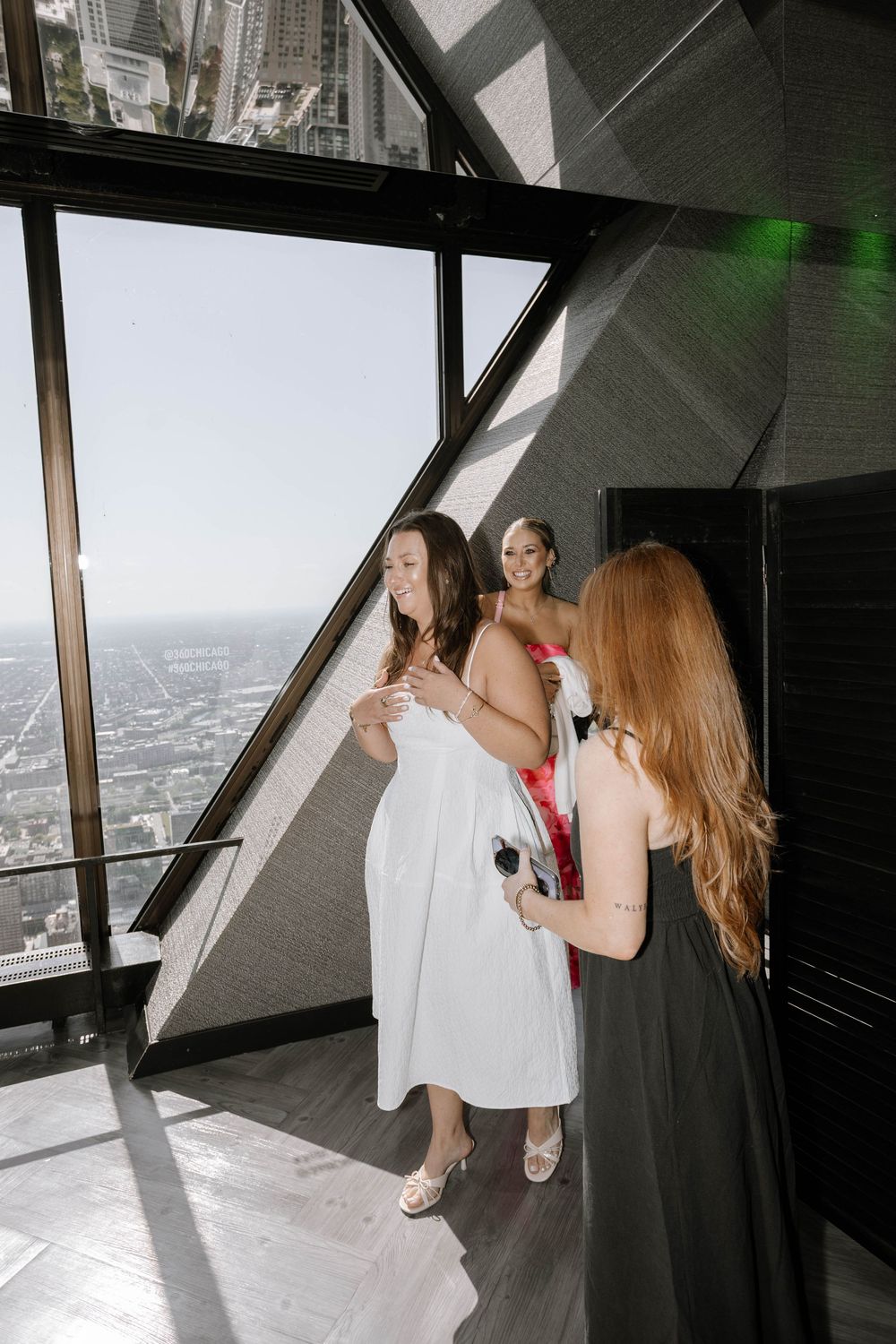 Three friends in formal attire enjoy city views from a high-rise observation deck with dramatic lighting.