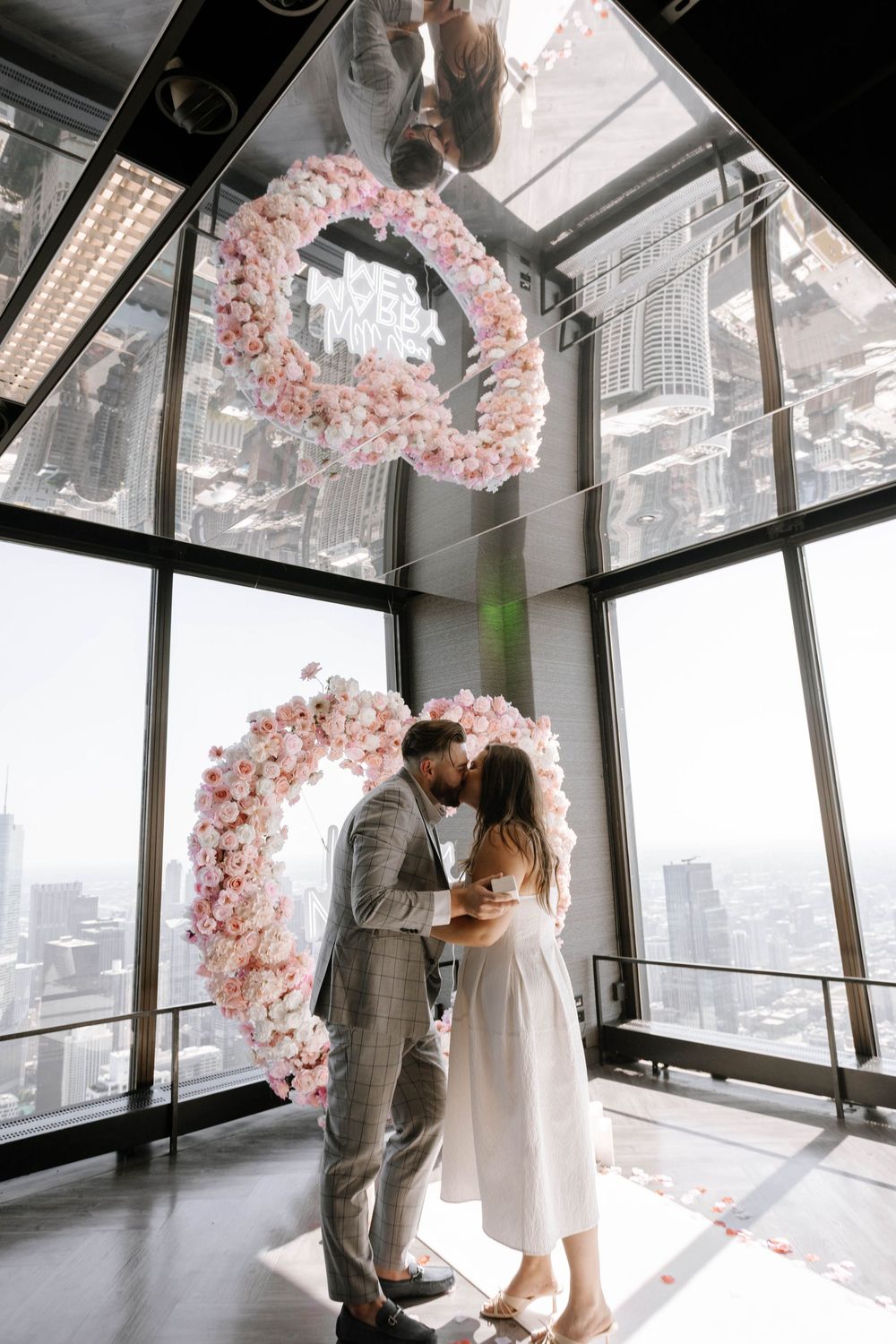A romantic proposal sequence in a modern venue with pink cherry blossom decor and cityscape views.