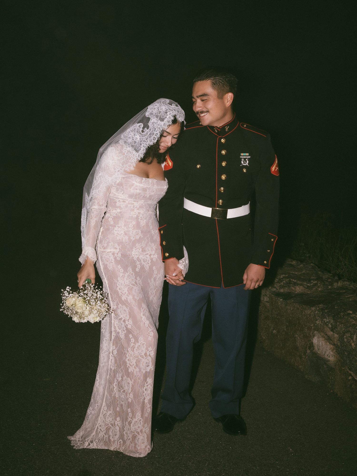 Wedding couple in formal attire standing together on a dark path.