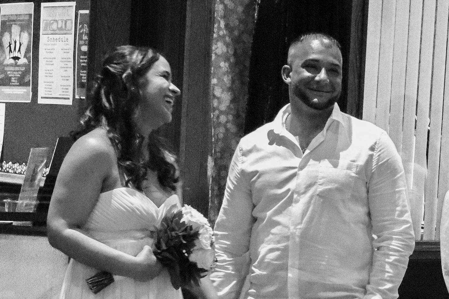 Wedding couple standing in white attire outside building entrance.