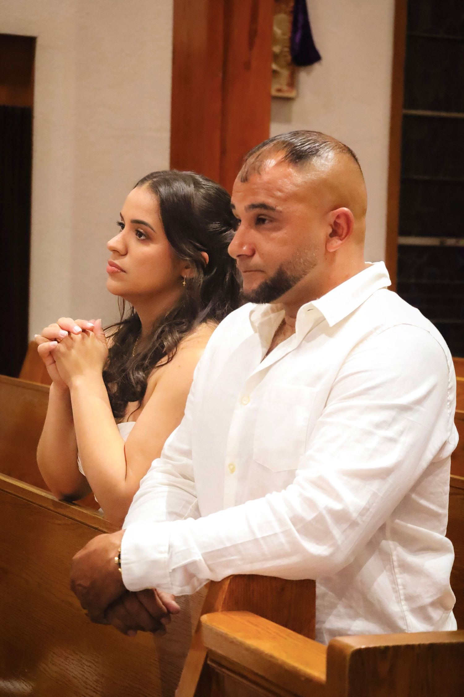Couple sitting together in church pews during wedding ceremony service.