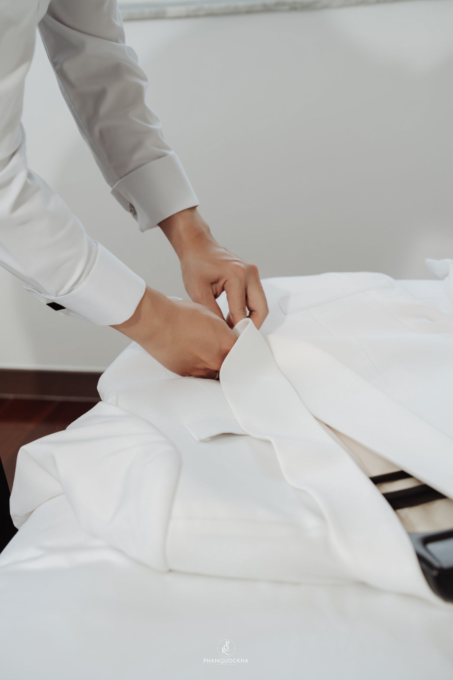 Groom in grey shirt carefully folding white dress shirt on a bed before wedding ceremony.