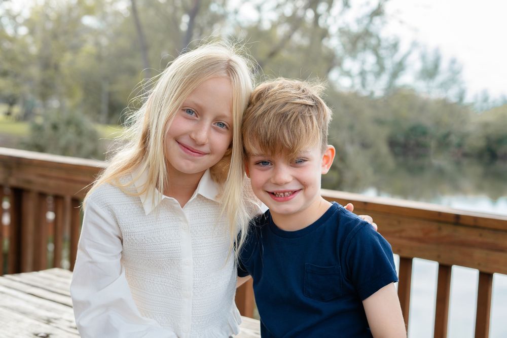 Children sitting together on a wooden deck during a bright sunny day outdoors.