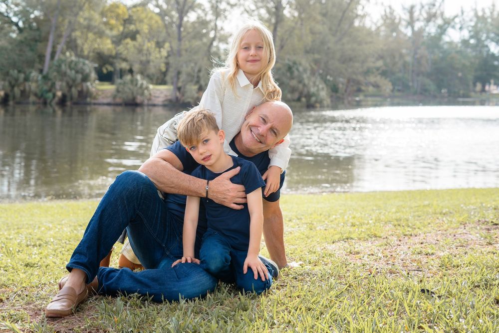 A family relaxing together on grass near a lakeside setting during an outdoor photo session.