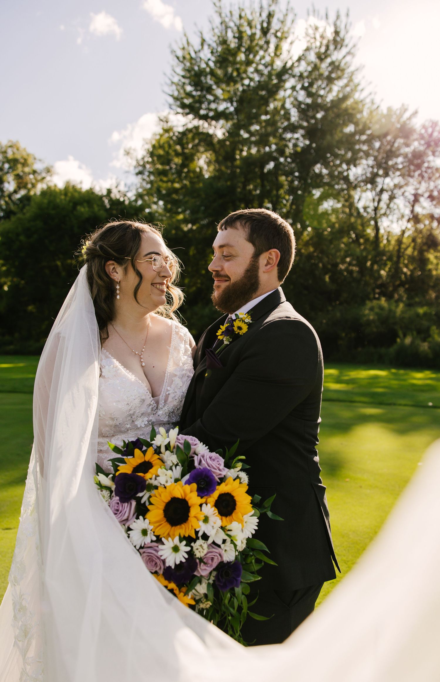 Newlywed couple walking together on lush green golf course with flowing white wedding dress trailing behind them.