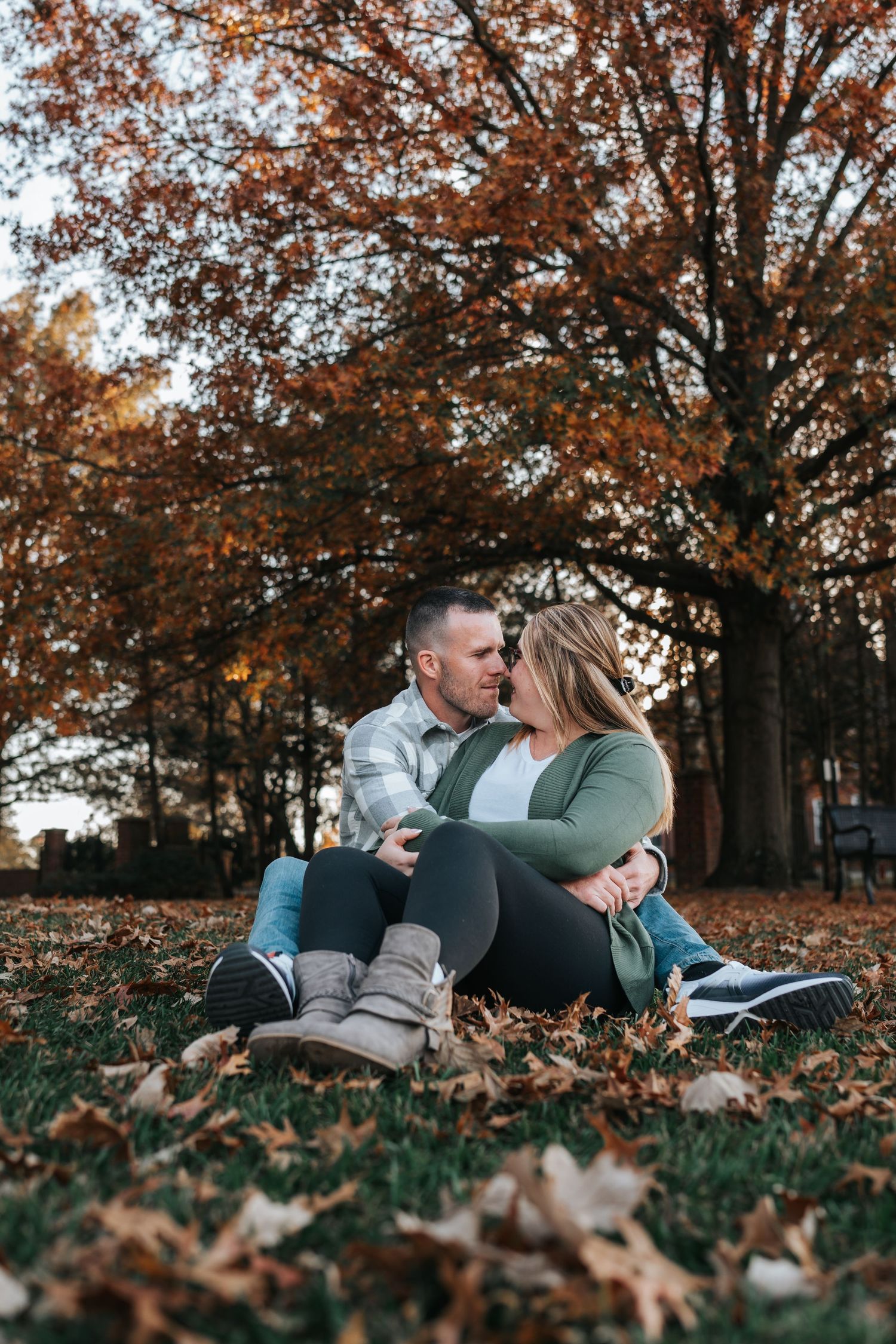 Couple sitting together among fallen autumn leaves beneath a colorful maple tree.