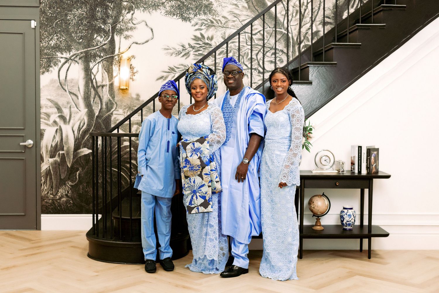A group wearing coordinated blue outfits poses on stairs with a decorative wall mural.