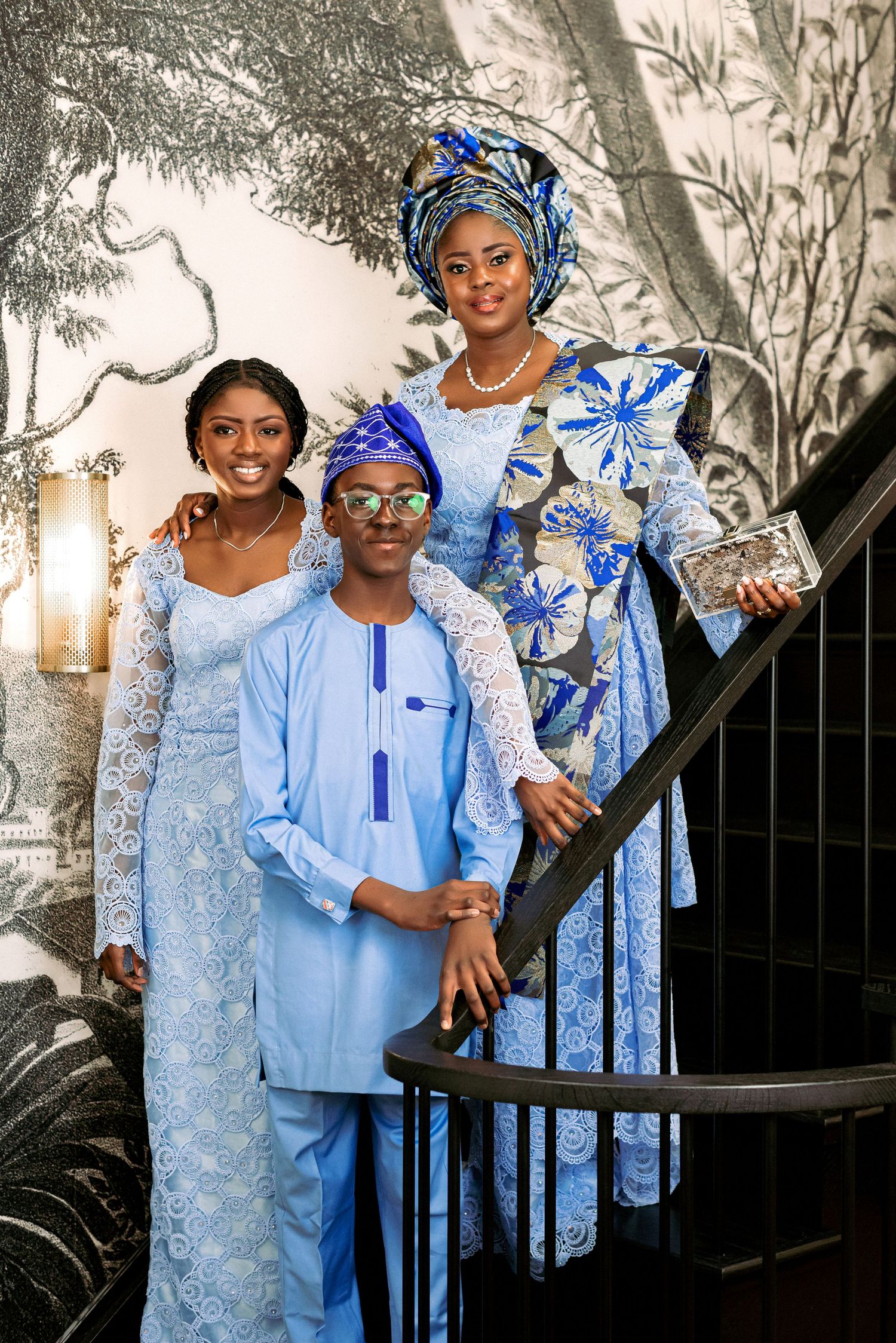 Three people in matching blue and white traditional African attire pose on a staircase.