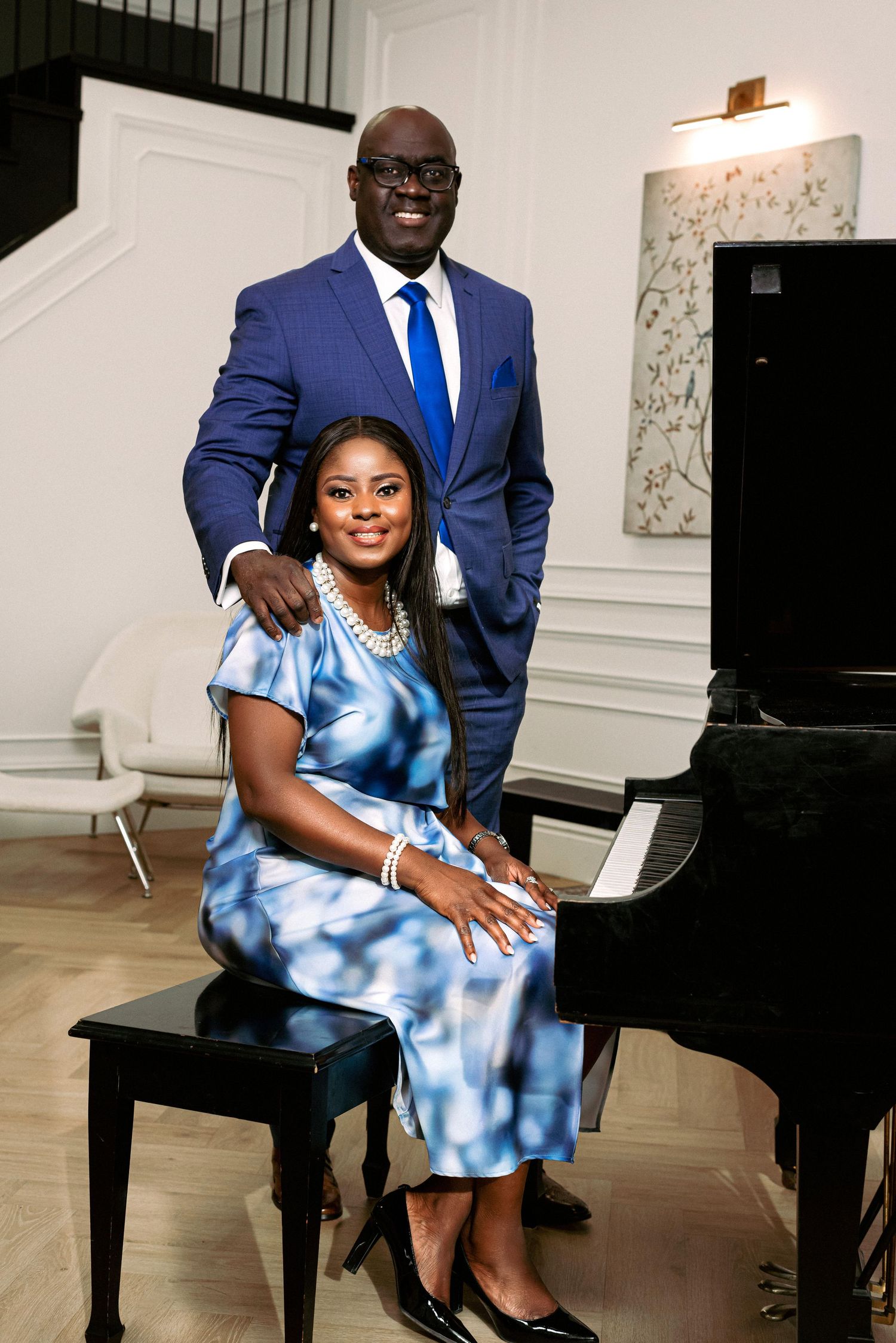 A couple poses elegantly by a grand piano, with one seated at the bench.