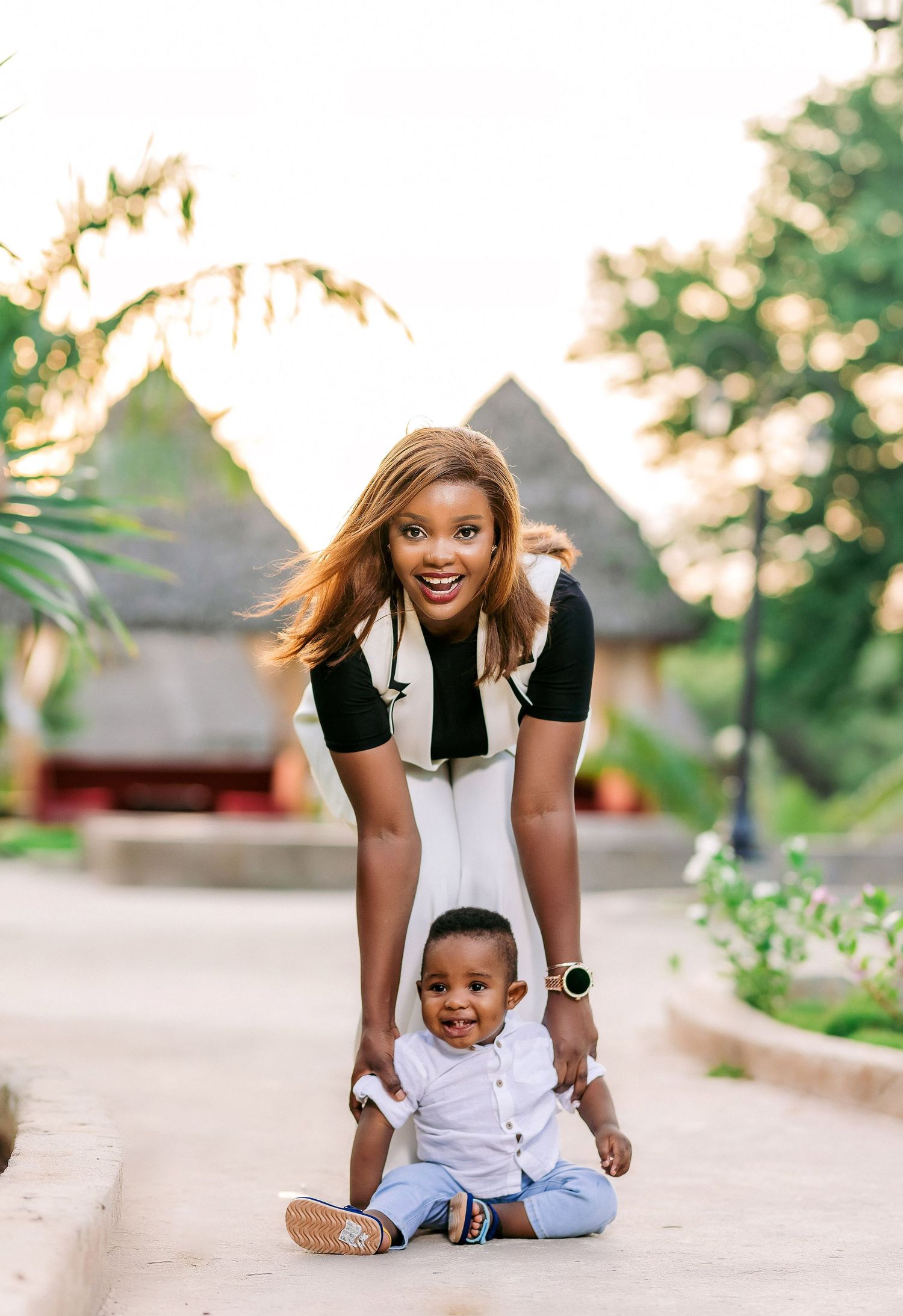 A playful outdoor portrait of parent and child sitting together at sunset with gazebos in background.