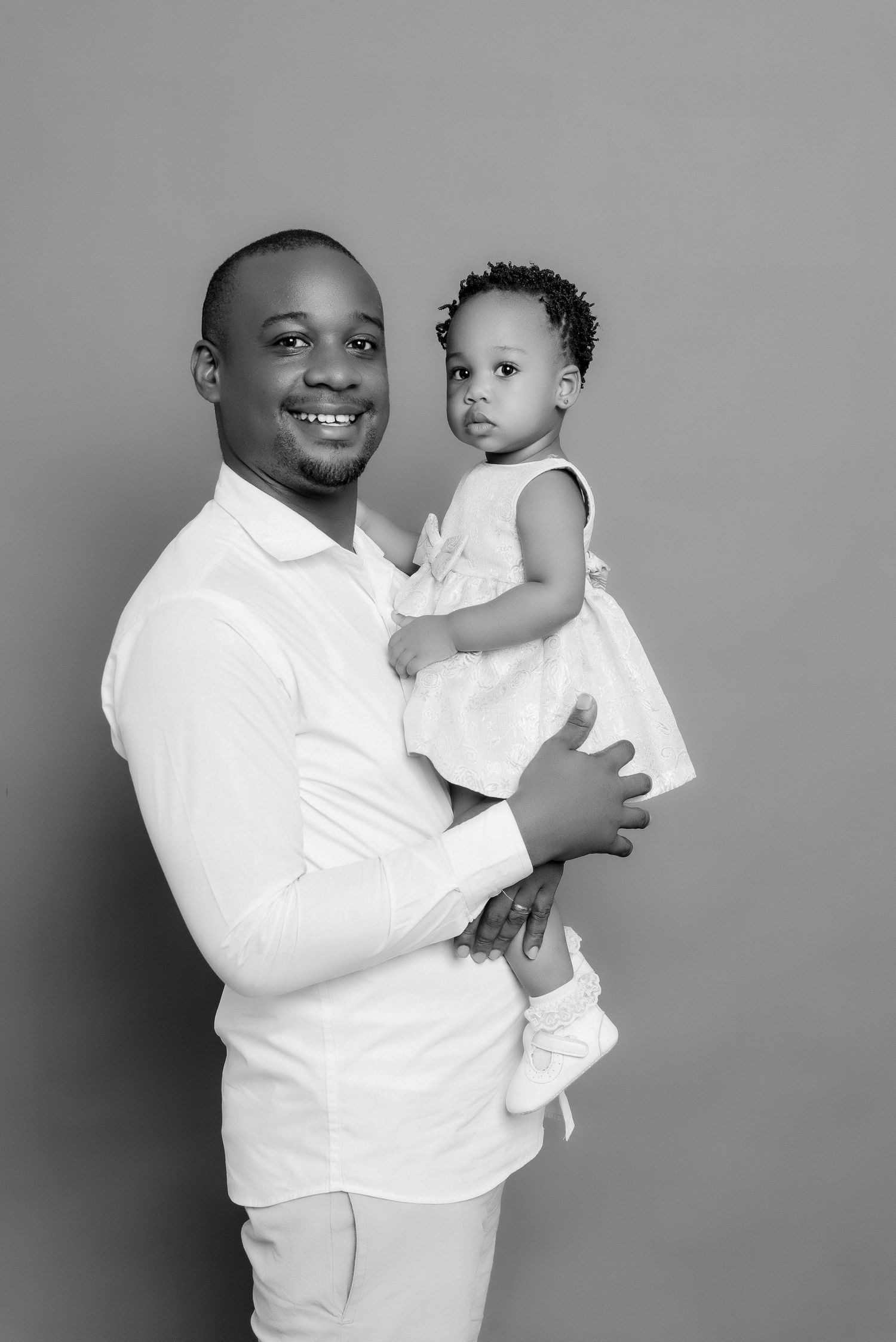 Black and white studio portrait of parent holding small child in white dress.