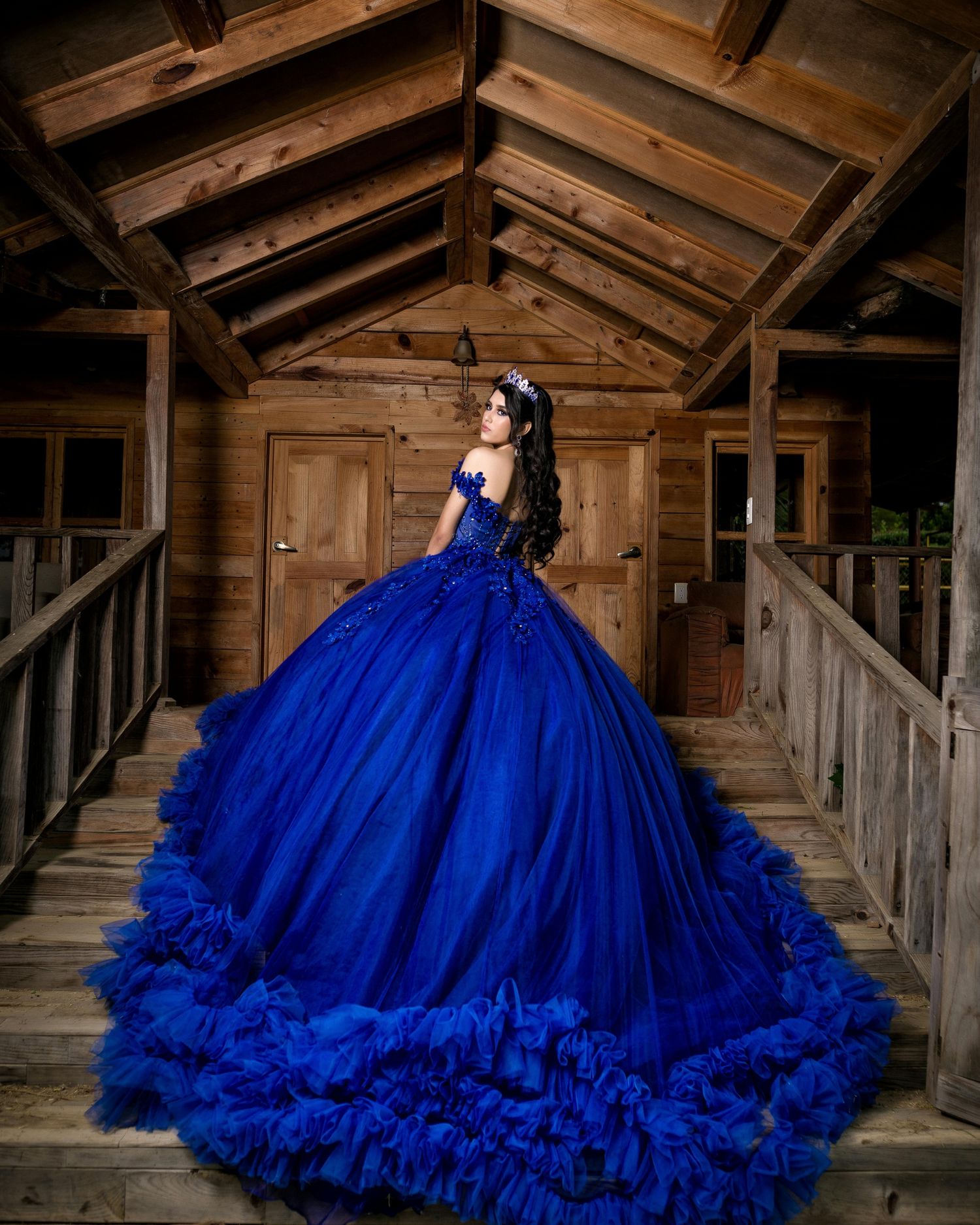Vibrant royal blue ball gown with dramatic ruffled skirt shown in rustic wooden setting.