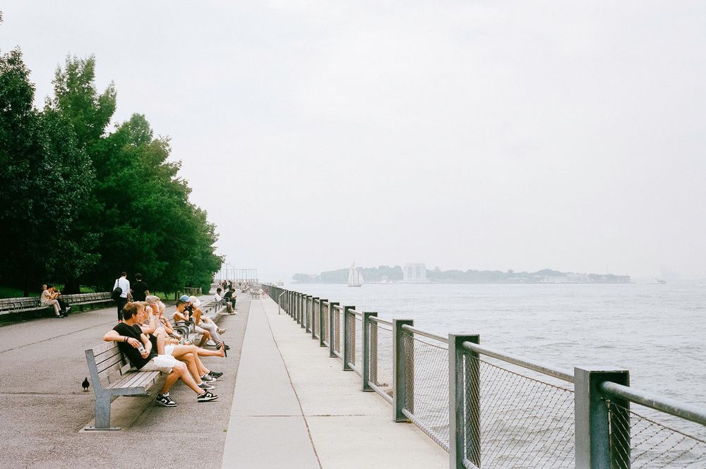 Panoramic view of people enjoying a scenic coastal promenade on a cloudy day with cityscape visible in the distance.