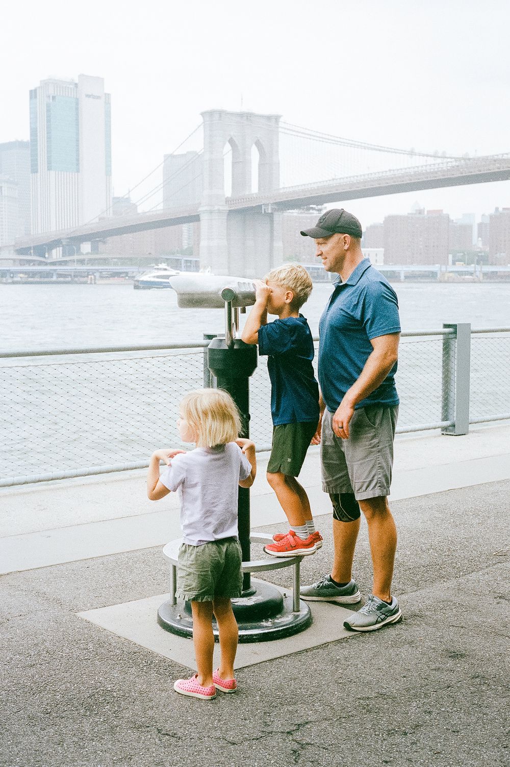 Family sightseeing at Brooklyn Bridge viewpoint with scenic Manhattan skyline and East River in New York City.