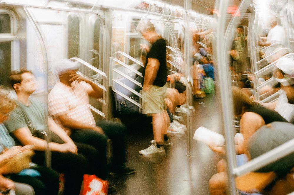 People sitting in motion-blurred subway train car with white poles and windows creating a dynamic commuting scene.