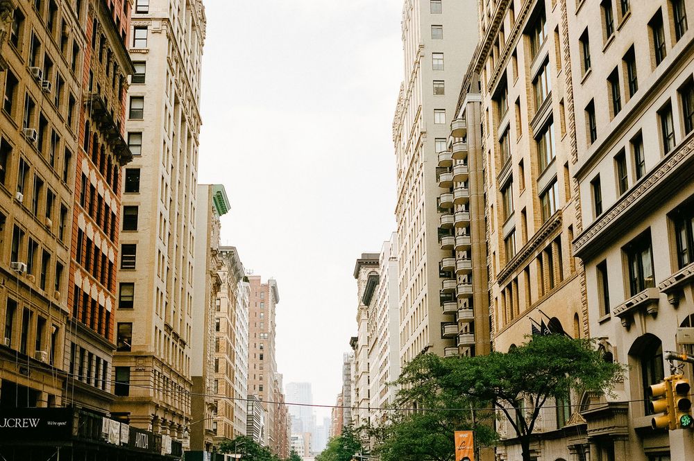 Urban street view of tall apartment buildings and office towers along a tree-lined avenue in Manhattan, New York City.