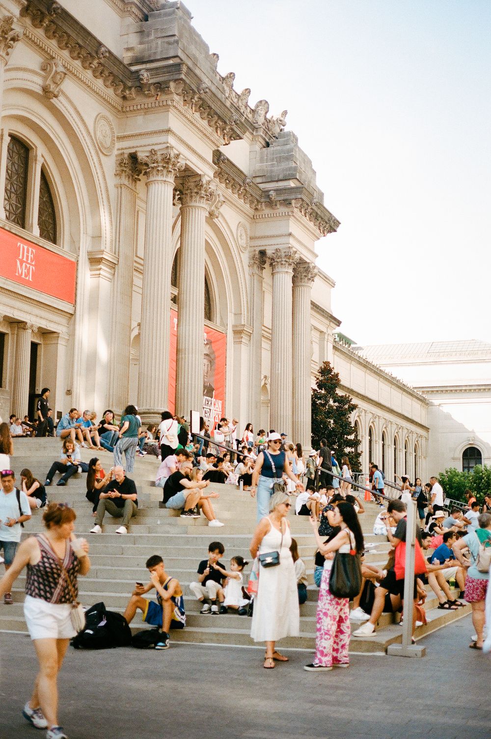 People gathering and sitting on the grand steps of the Metropolitan Museum of Art in New York City.
