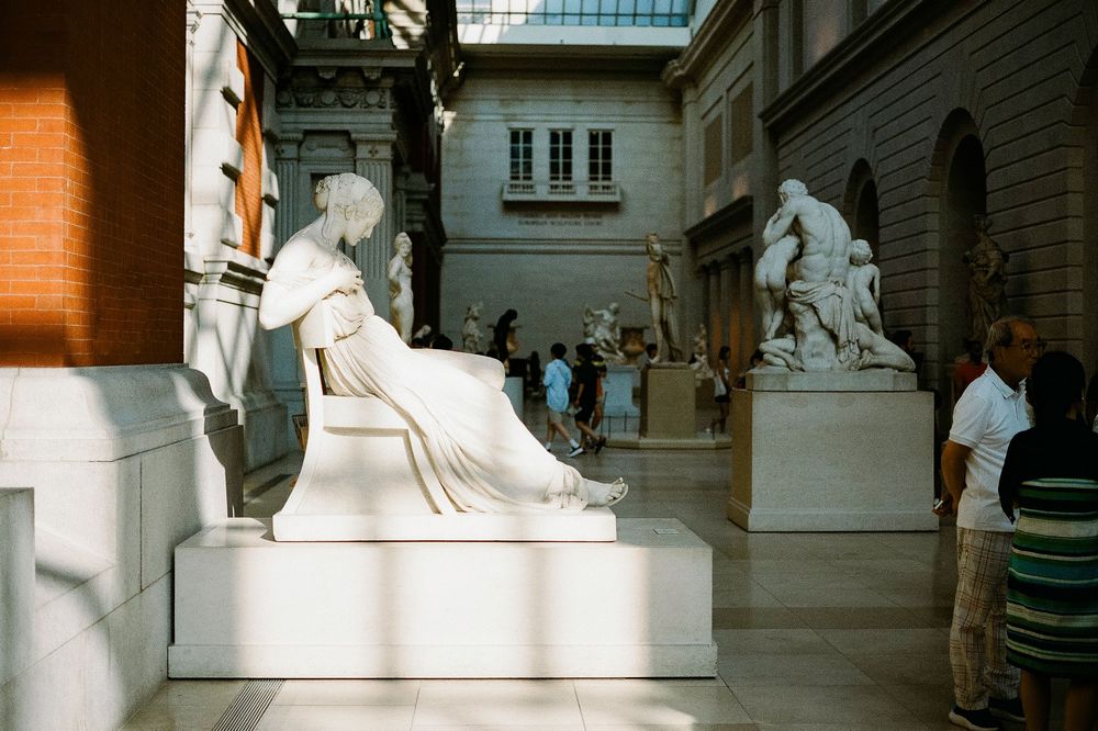 Marble sculptures displayed in a gallery hallway illuminated by natural light streaming through tall windows.